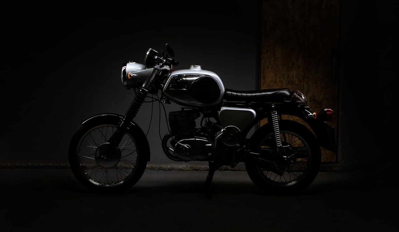 A vintage motorcycle parked in a dark studio room, lit only by directional warm light