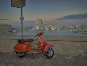 a red scooter parked next to a wall near a body of water