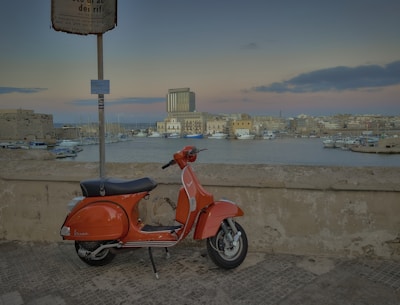 a red scooter parked next to a wall near a body of water