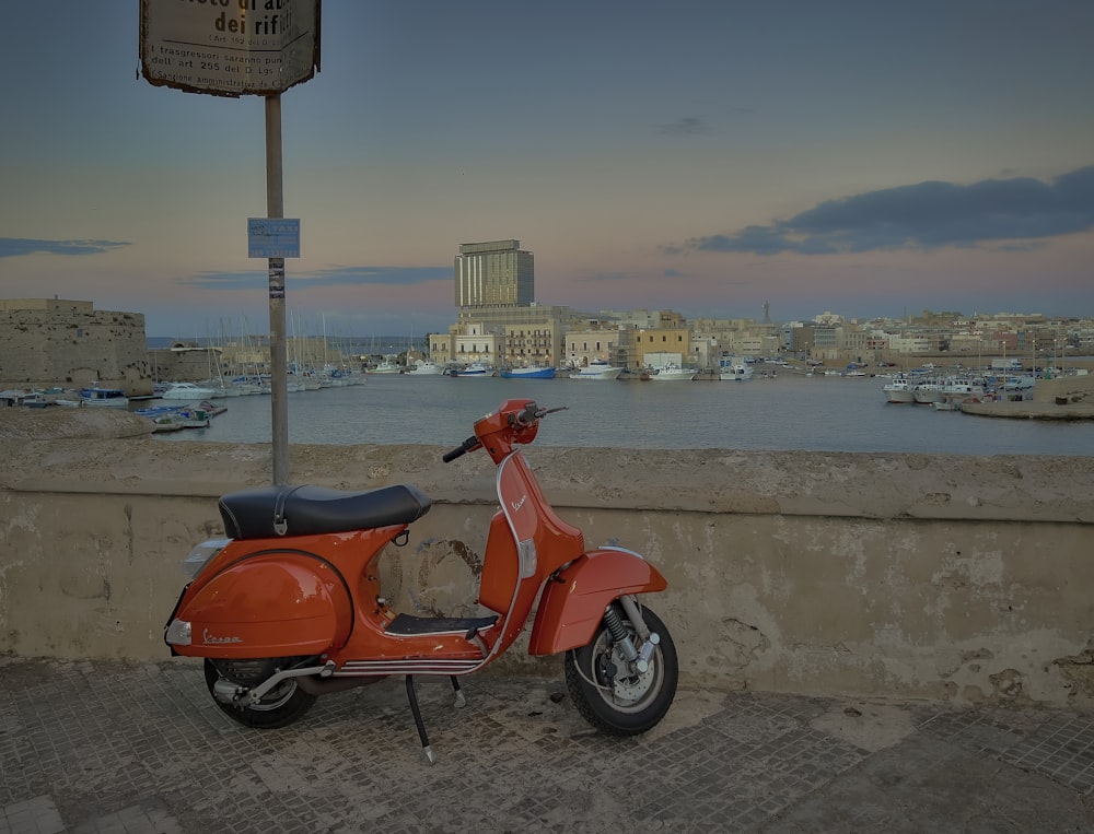 a red scooter parked next to a wall near a body of water