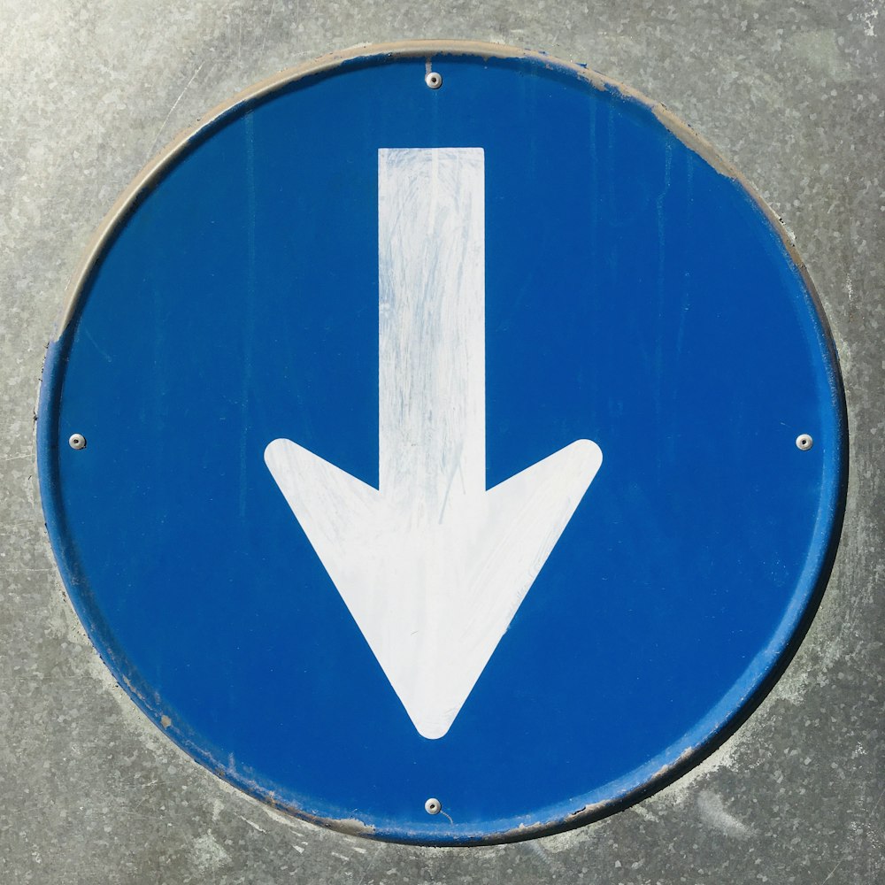 Un primer plano de un letrero azul con una flecha blanca