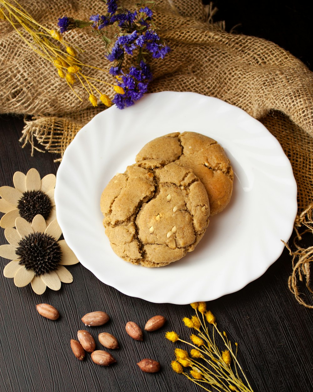 two cookies on a white plate next to dried flowers