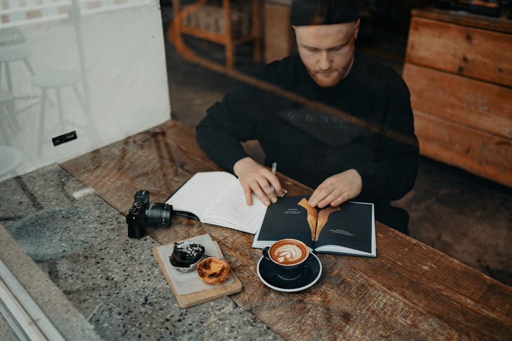 a man sitting at a table with a book and a cup of coffee