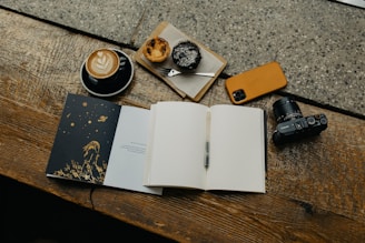 an open book sitting on top of a wooden table next to a cup of coffee