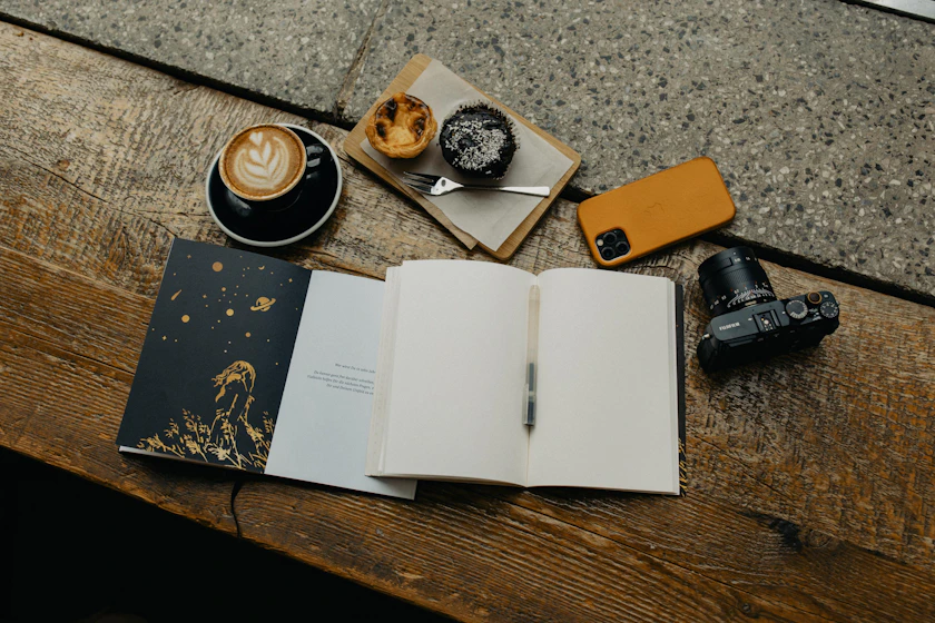 an open book sitting on top of a wooden table next to a cup of coffee