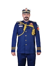 A person is wearing a formal military or naval uniform with a white and blue cap. The uniform is primarily navy blue, adorned with various gold accents including epaulettes, buttons, and decorative cords. There are multiple badges and insignia on the chest and arms, and a flag patch on the right sleeve.