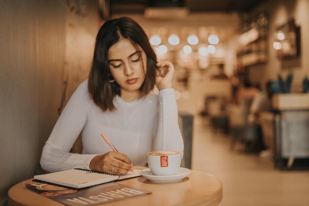 a woman sitting at a table writing in a notebook