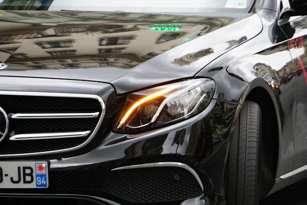 Close-up shot of a gleaming black luxury car reflecting soft golden light under a sleek urban backdrop.