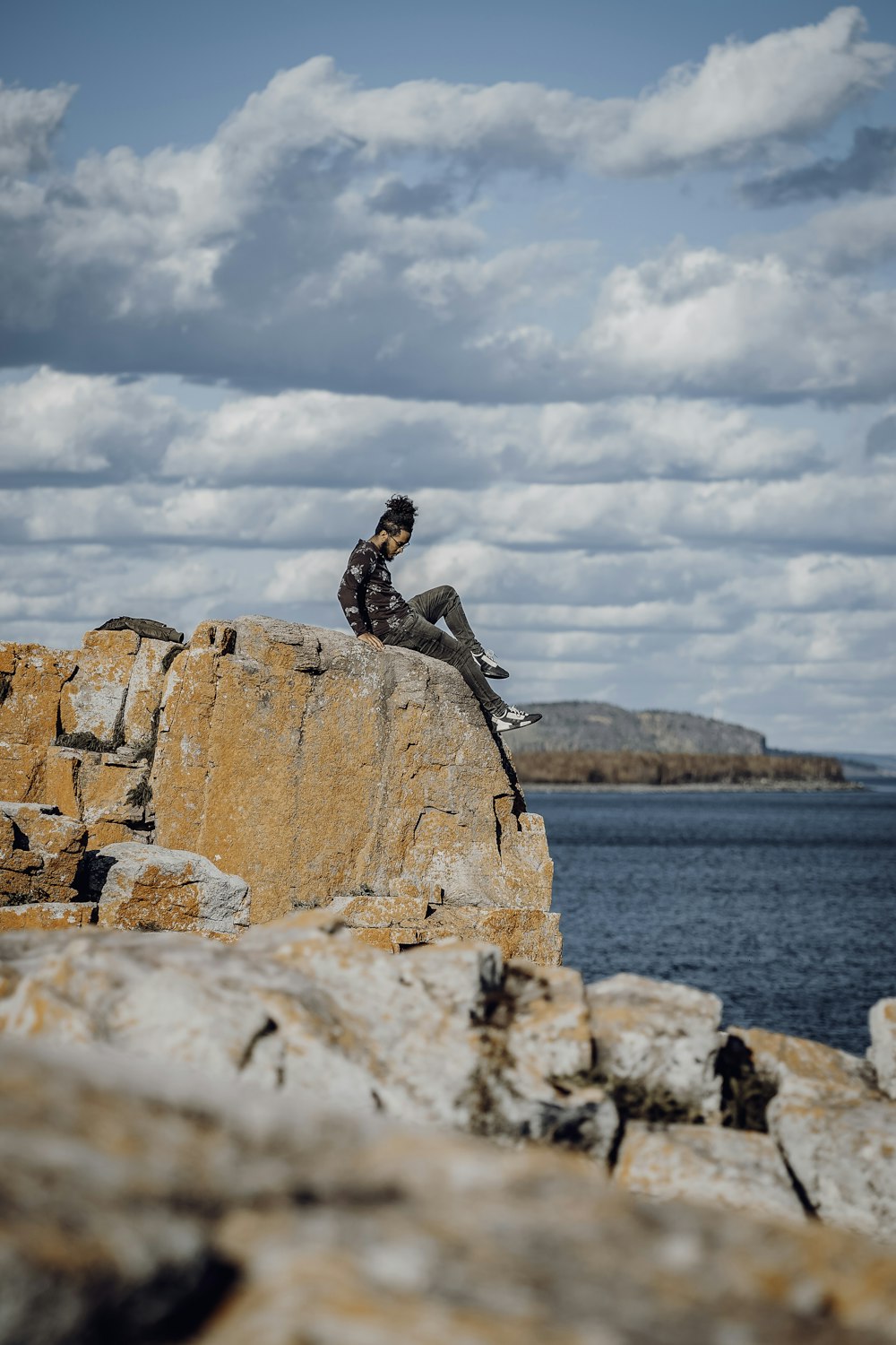 a man sitting on top of a rock next to the ocean