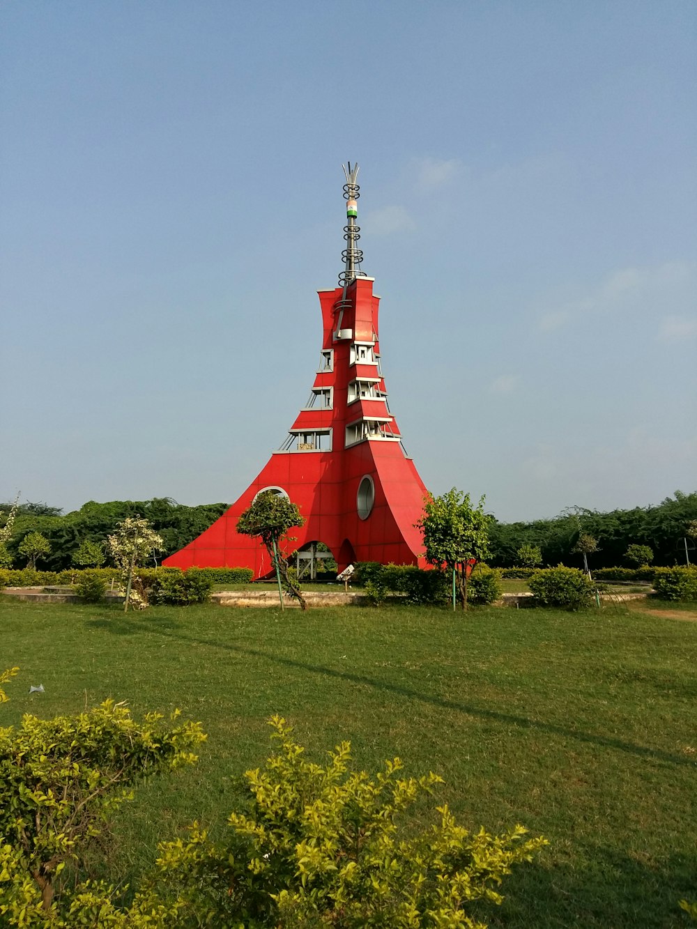 a very tall red tower sitting in the middle of a lush green field