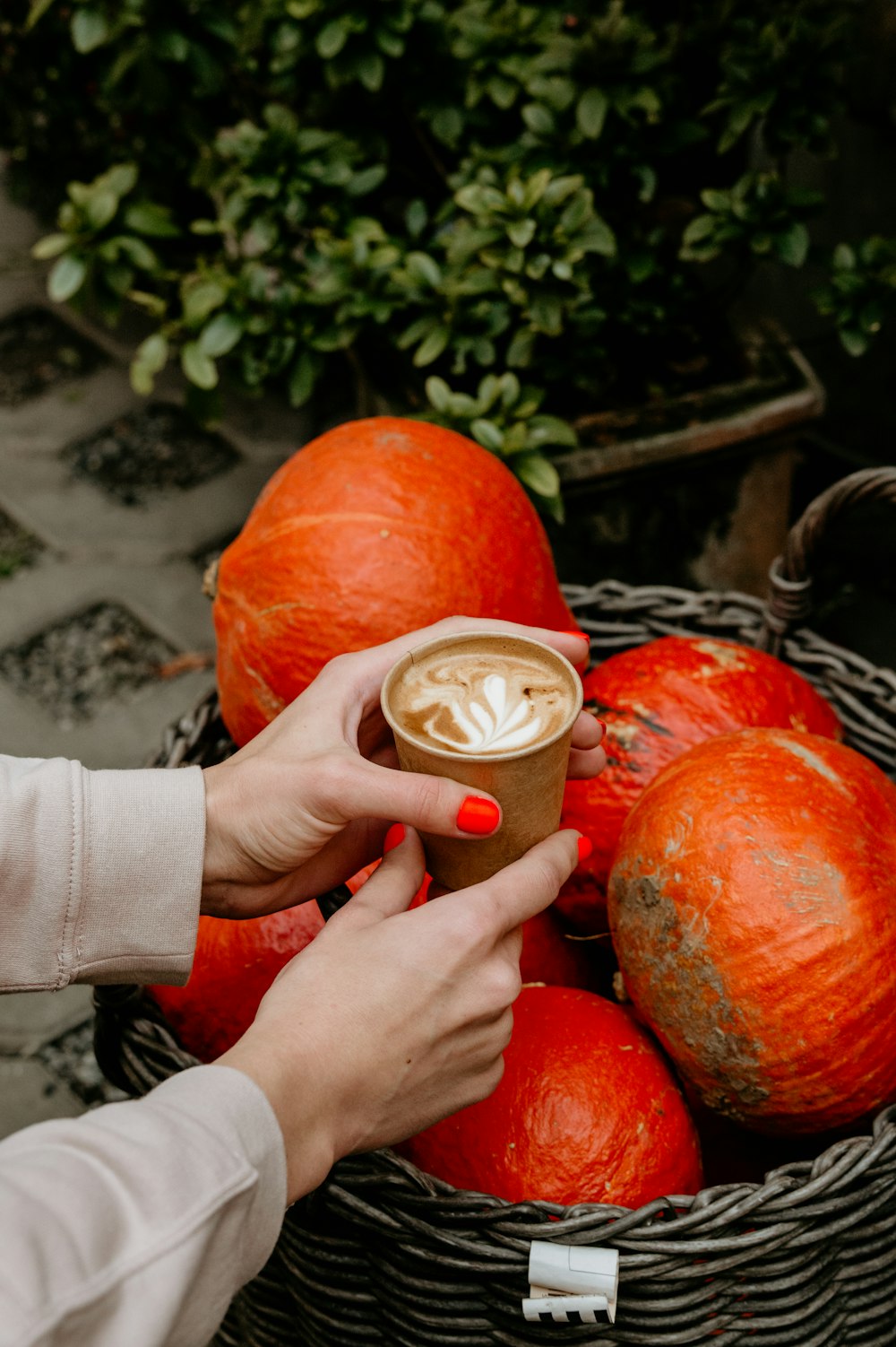 a woman holding a cup of coffee in front of a basket of pumpkins