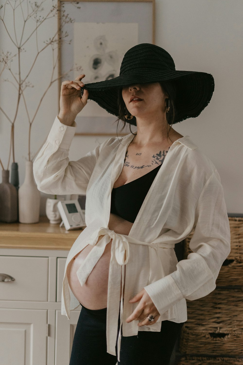 Una mujer embarazada con un sombrero negro fumando un cigarrillo