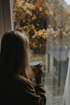 a woman holding a cup looking out a window