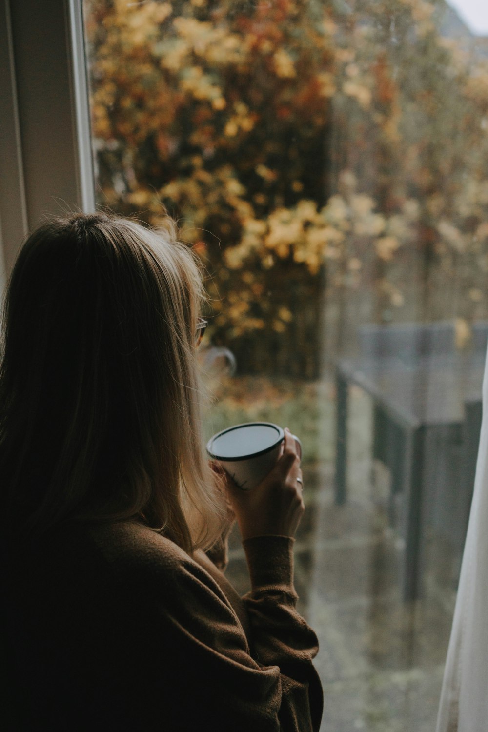 Eine Frau hält eine Tasse in der Hand und schaut aus dem Fenster