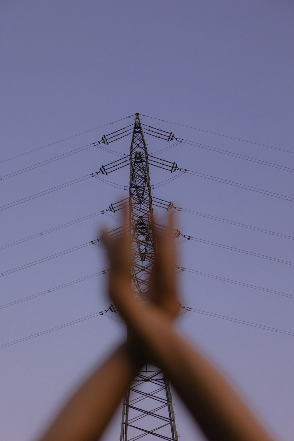 uma pessoa segurando as mãos para cima na frente de uma torre de alta tensão