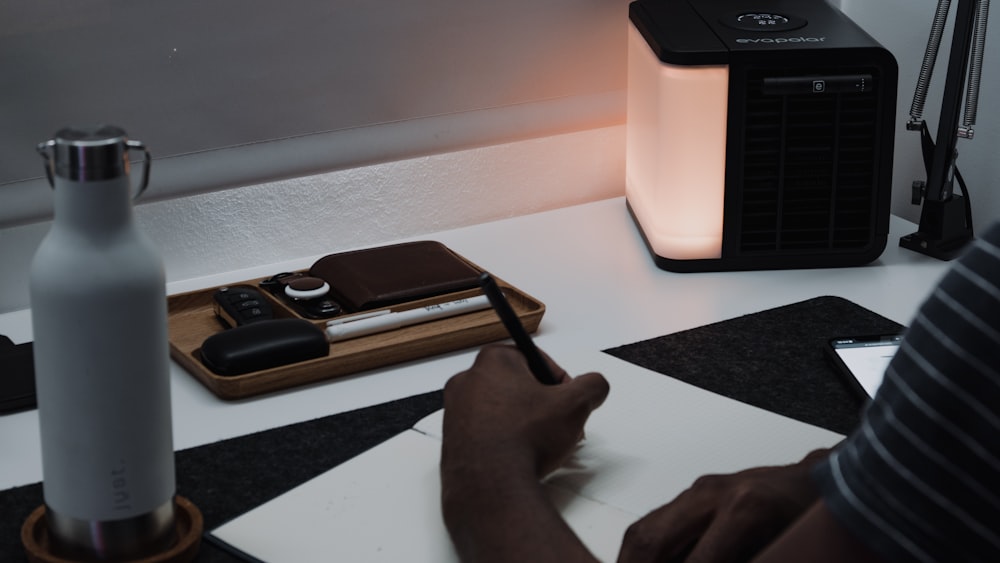 a person writing on a piece of paper next to a lamp