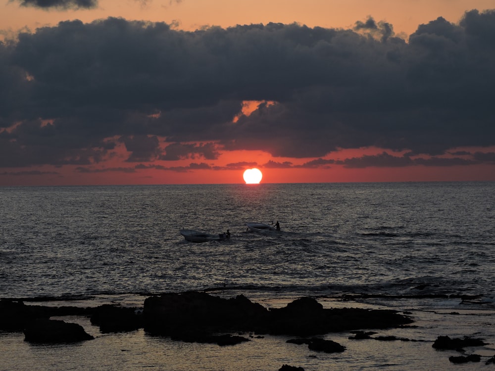 the sun is setting over the ocean with surfers in the water