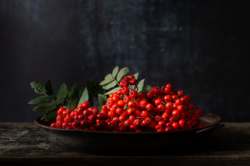 a bowl filled with red berries on top of a wooden table