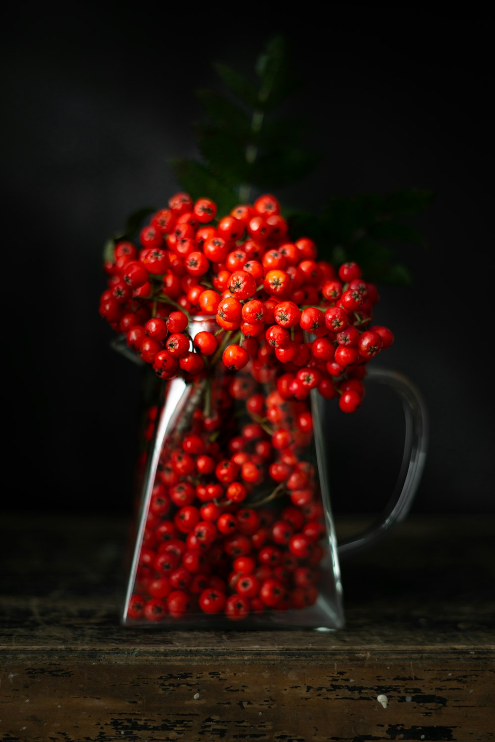 a glass vase filled with red berries on top of a table