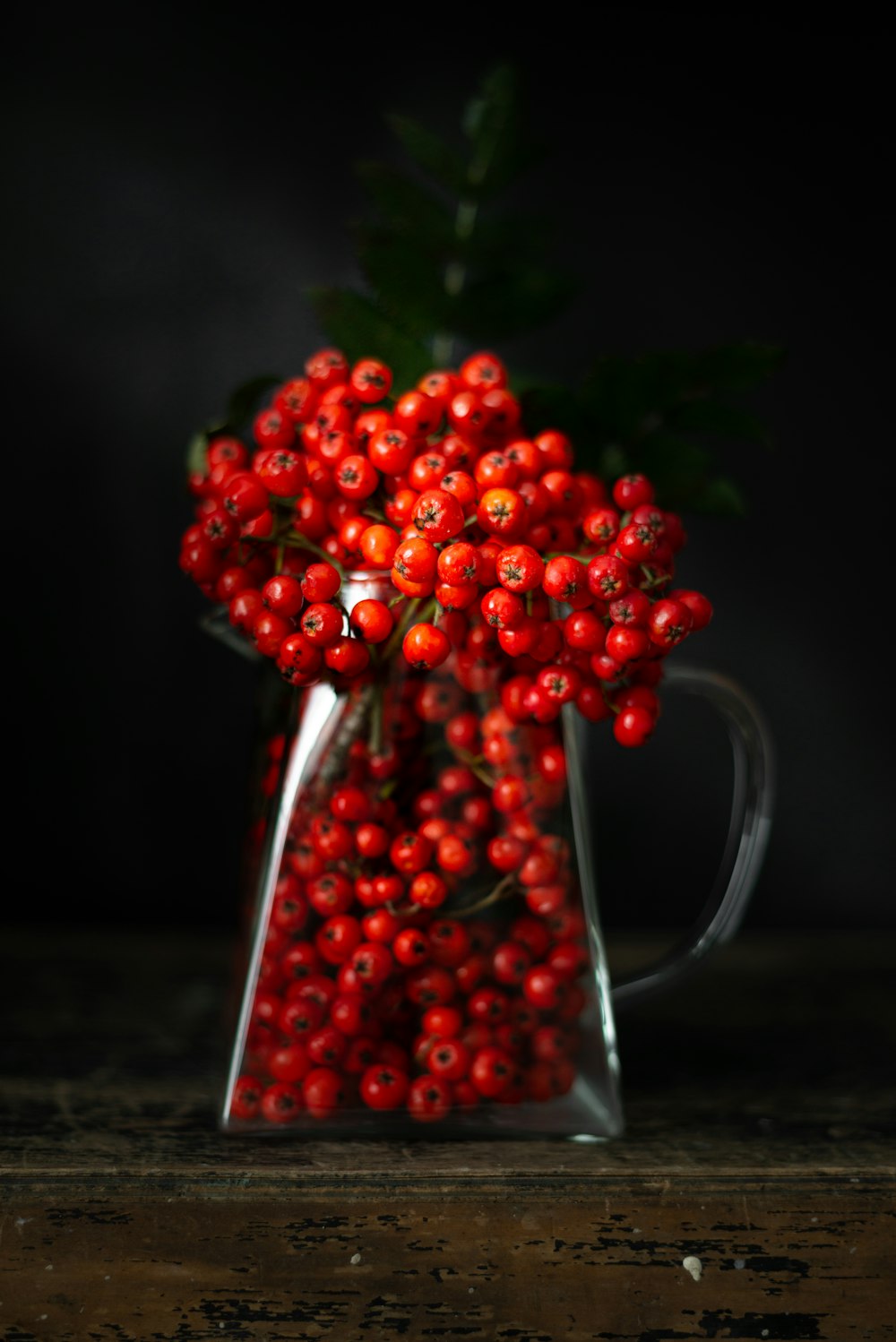 un vase en verre rempli de baies rouges sur une table