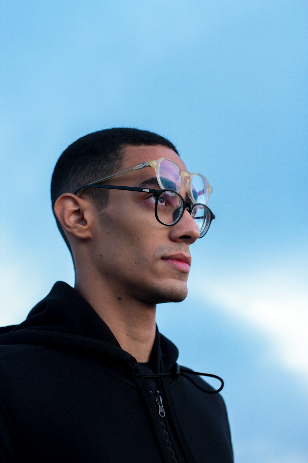 a young man wearing a pair of glasses against a blue sky