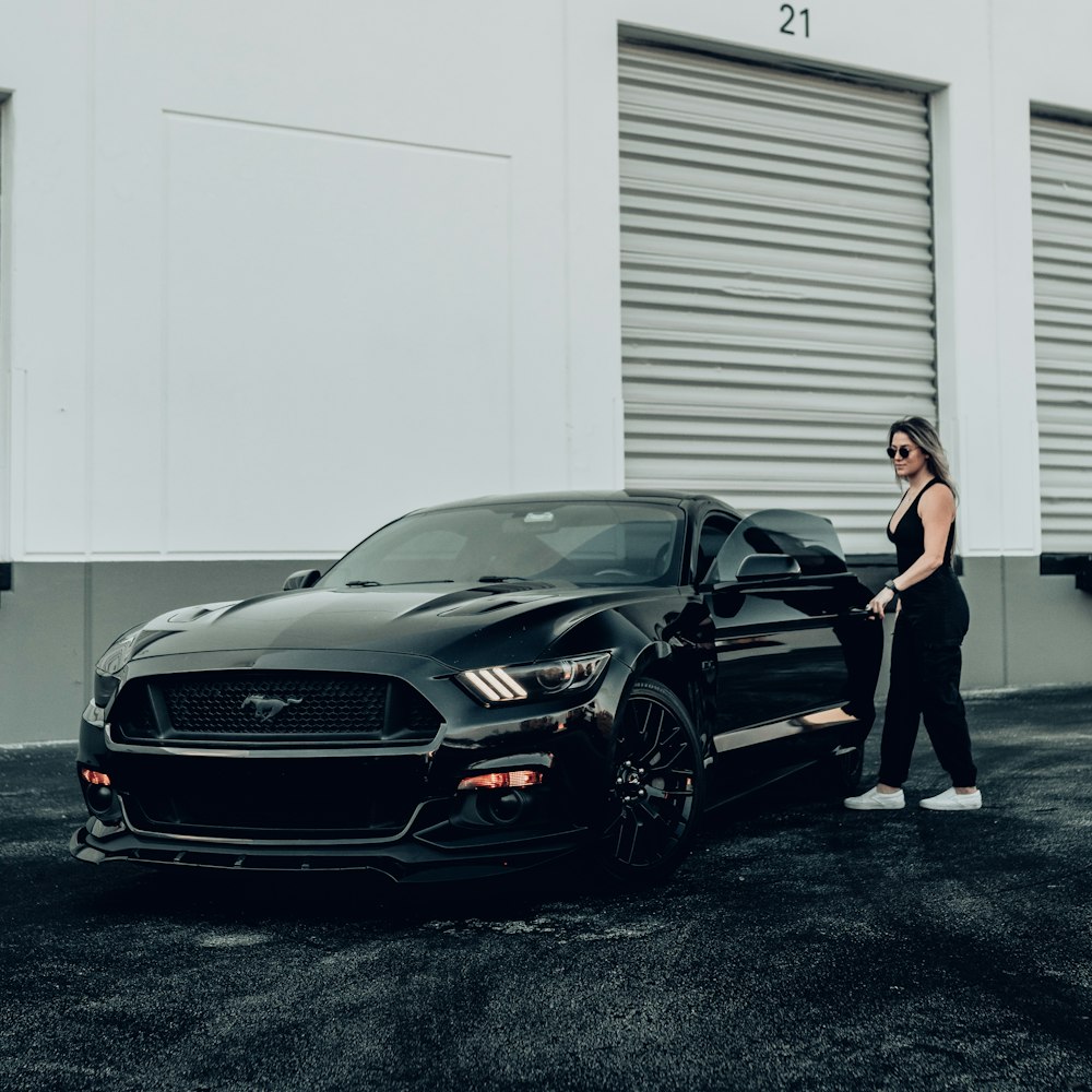 a woman standing next to a black car