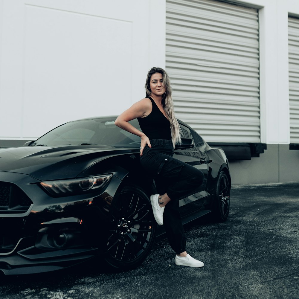 a woman standing next to a black sports car