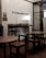 A cozy interior setting with wooden tables and chairs, characterized by minimalist black metal frames. The wall features a hashtag sign that reads '#TEMANSEJIWA' in a bold, simple font. The space has a small sign prohibiting smoking, and the overall ambiance is functional and modern, with a mix of wood and metal materials.
