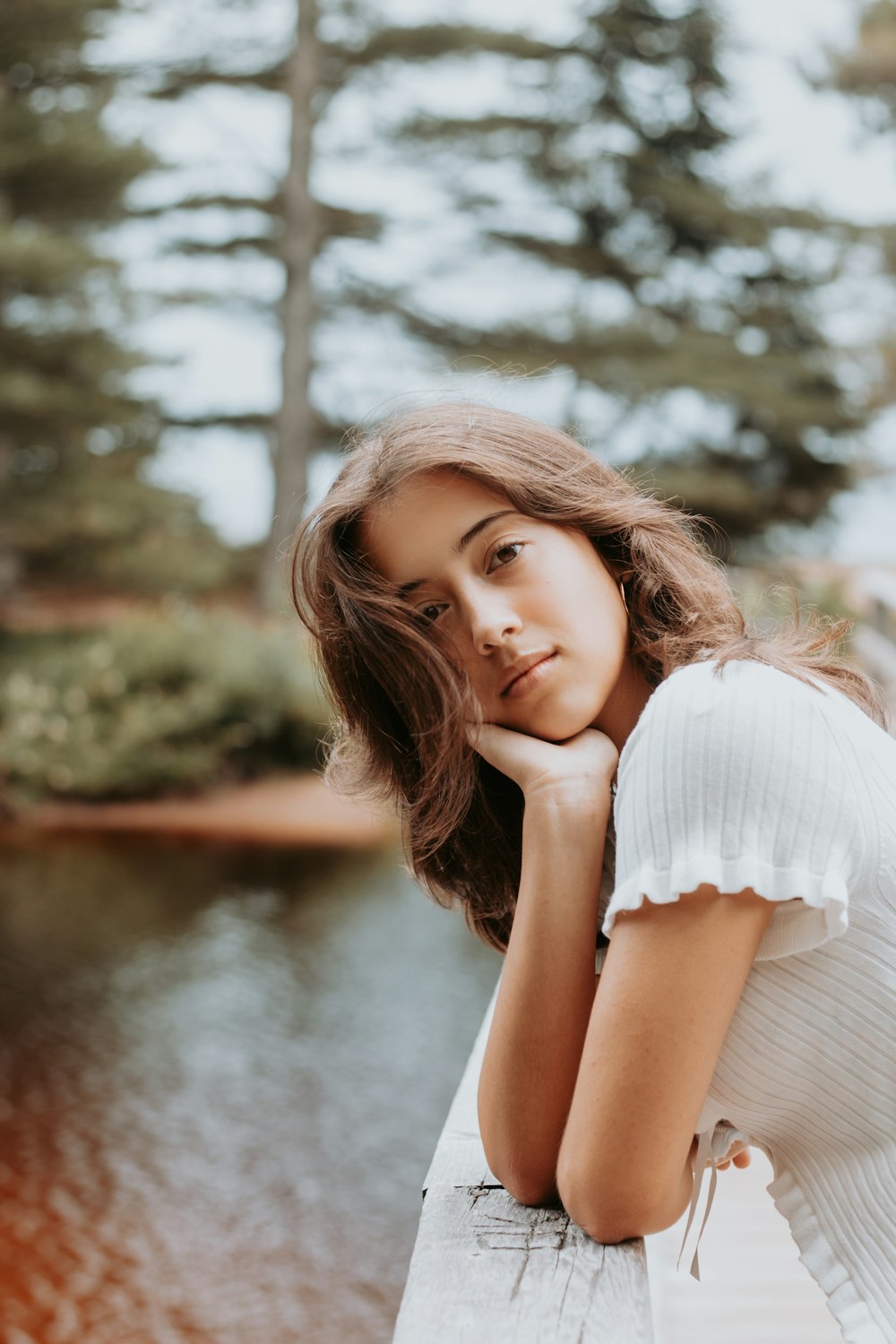 a woman leaning on a wooden fence near a body of water