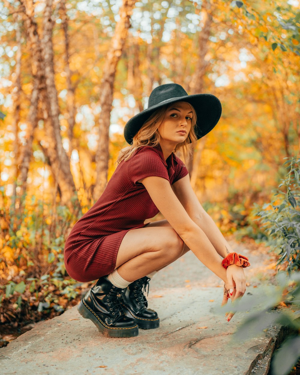a woman wearing a hat and boots crouching on a rock