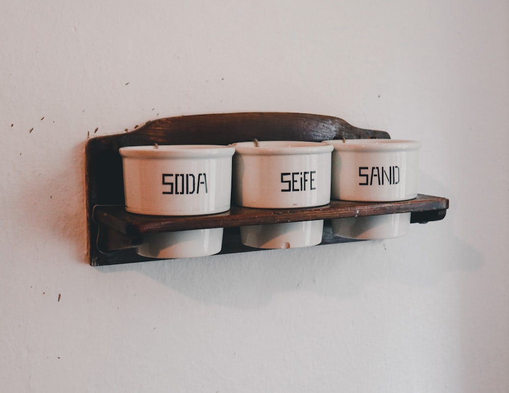 three coffee cups on a shelf with the words sand and surf written on them