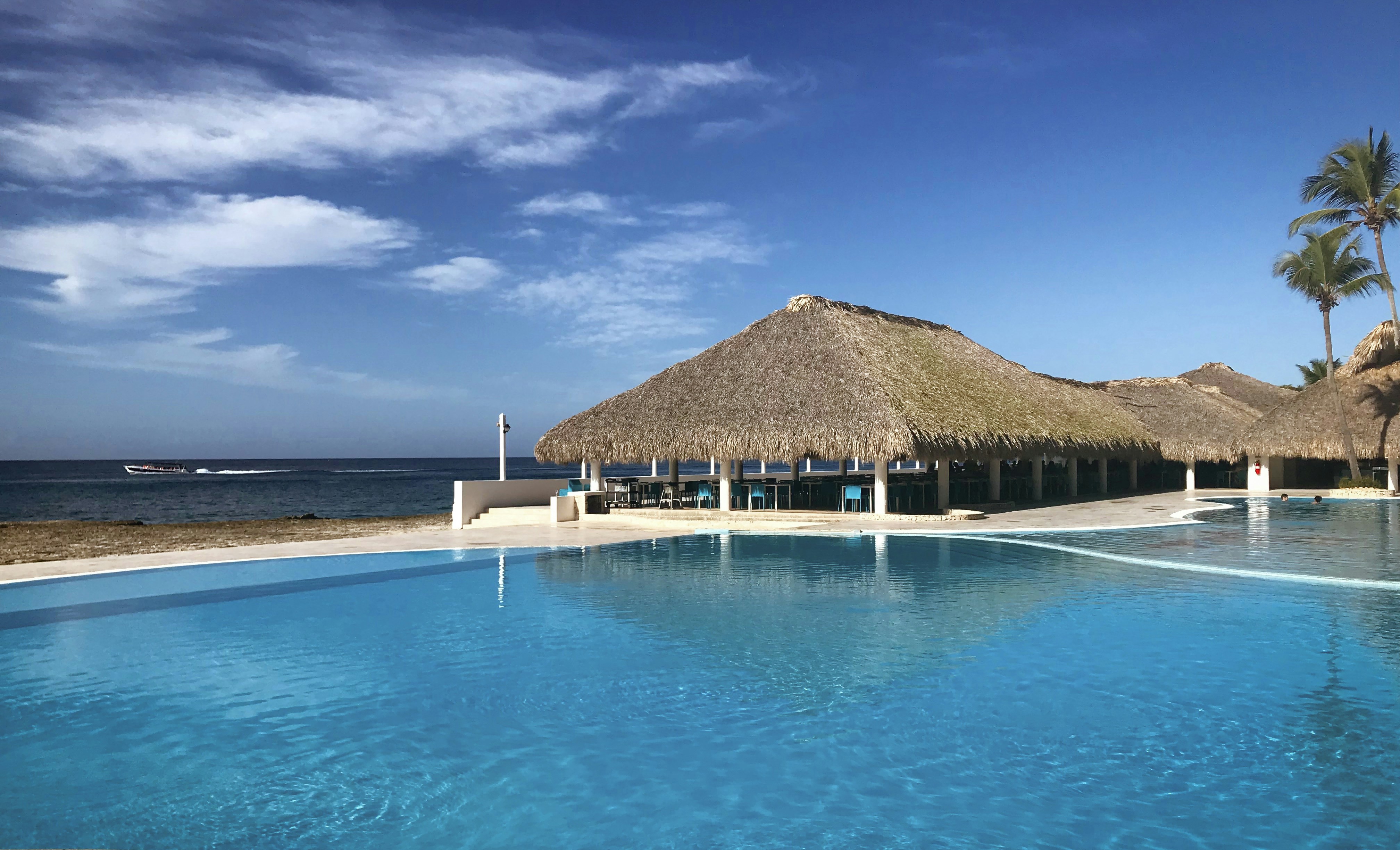 a large pool with a thatched roof next to the ocean