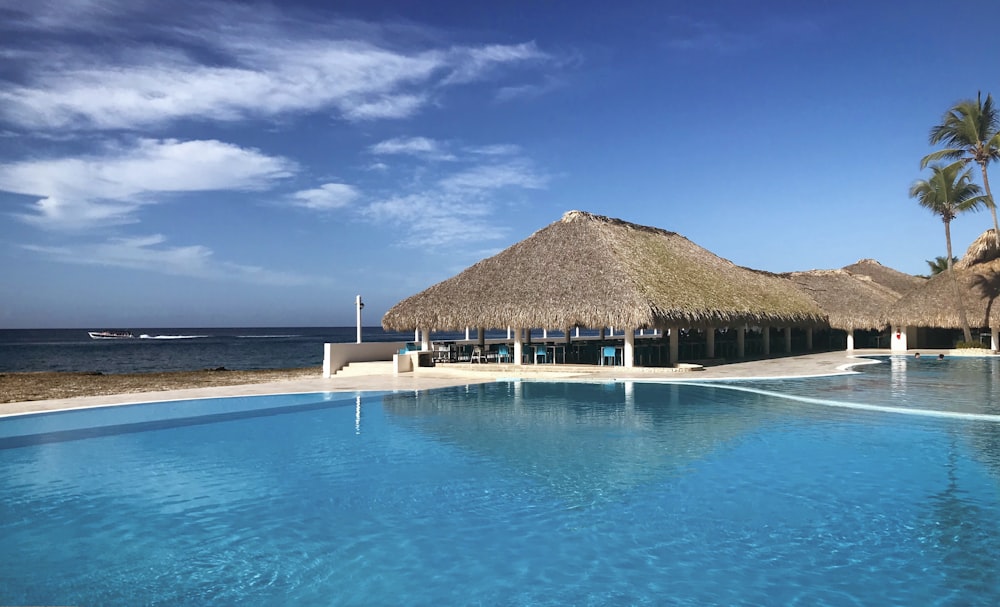 a large pool with a thatched roof next to the ocean