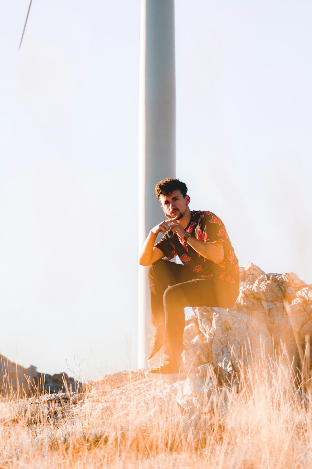 a man sitting on top of a rock next to a wind turbine