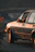 Close-up of a weathered vintage car against a backdrop of rustic wooden beams and soft evening light.
