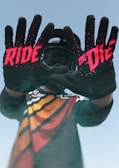 Gloved hands gripping motorcycle handlebars with a red and black jersey visible.