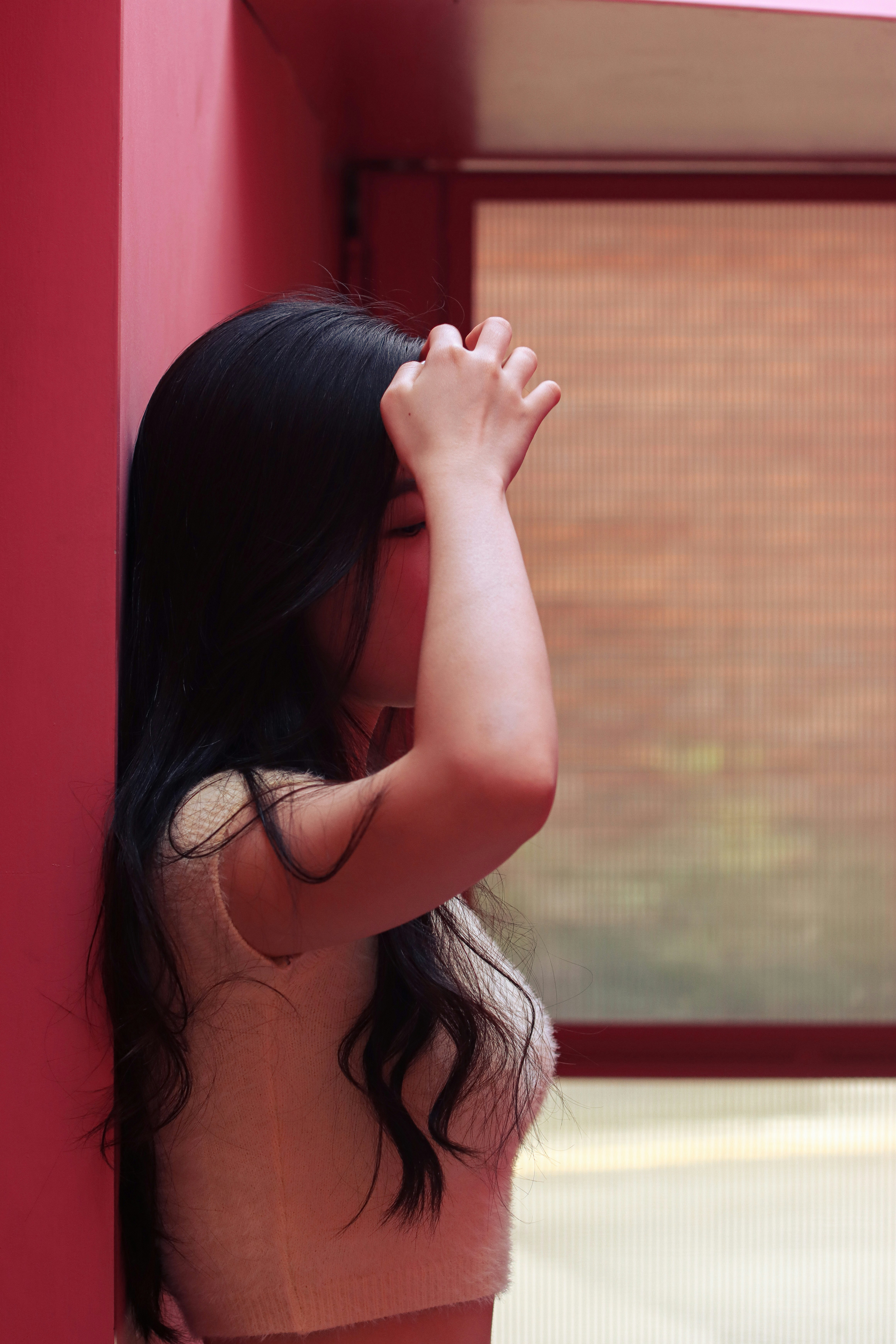 a woman leaning against a red wall with her hand on her head