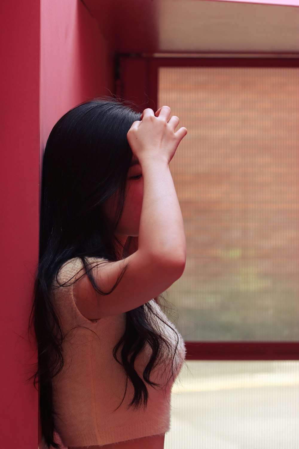 a woman leaning against a red wall with her hand on her head