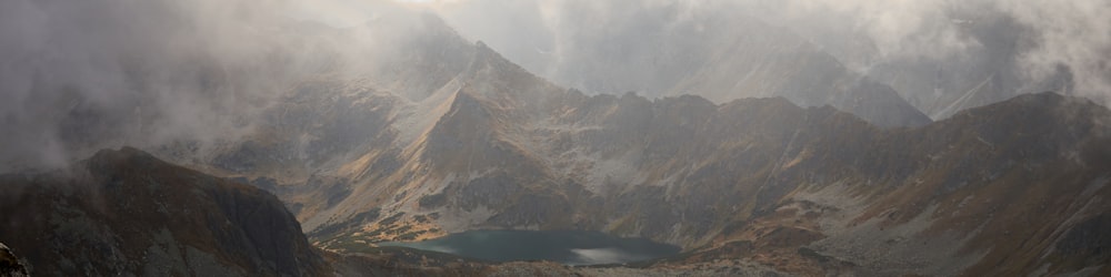 a mountain range with a lake surrounded by clouds