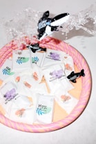 Several biodegradable product packages are arranged in a colorful inflatable pool. An inflatable whale toy is splashing water, creating a dynamic and playful scene. The packages are designed with various pastel colors, indicating different features or scents.