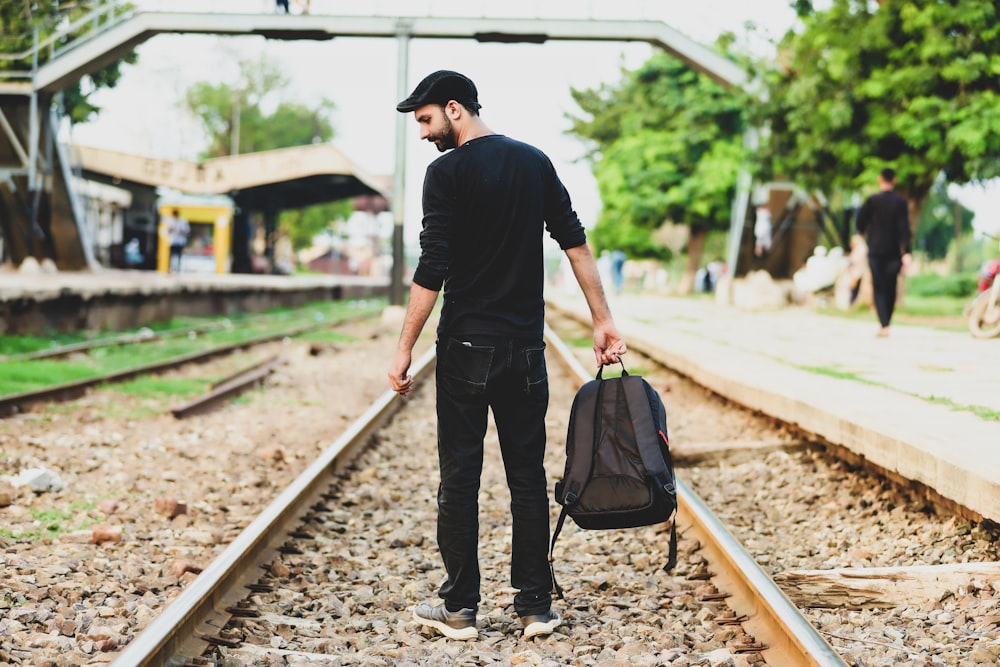 a man walking down a train track with a backpack