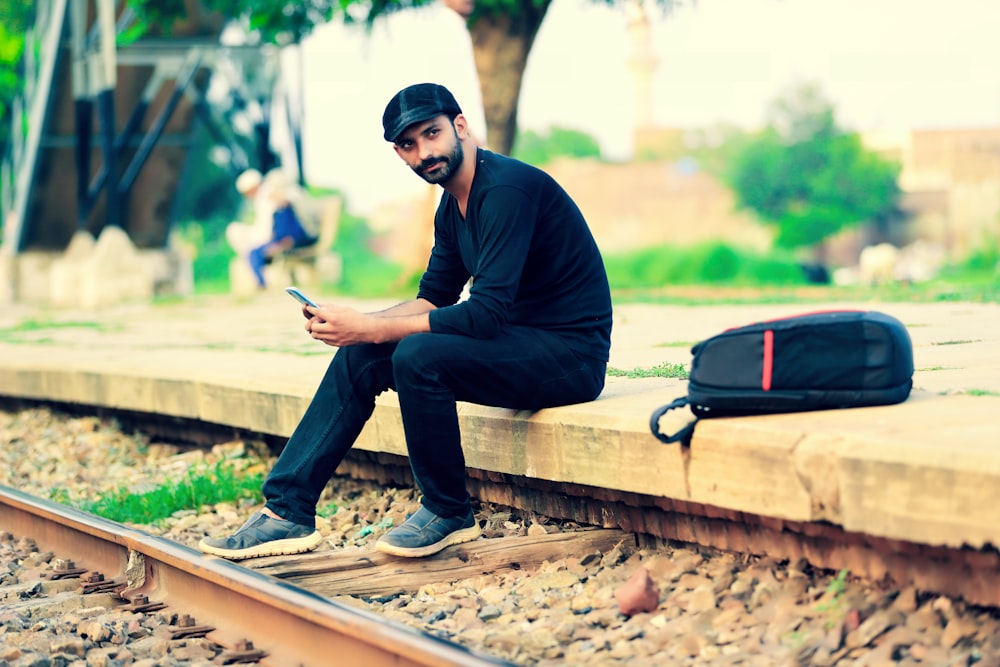 a man sitting on a train track looking at his cell phone