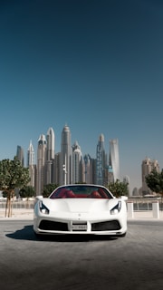 White sports car gleaming under a bright Middle Eastern city sky.