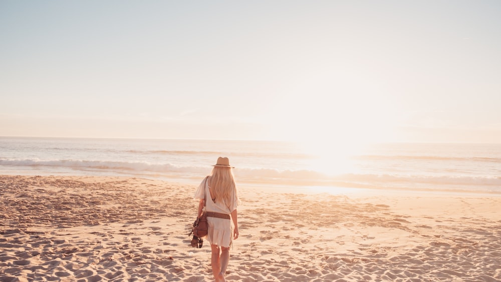 a woman in a white dress is walking on the beach