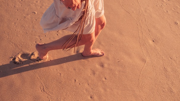 A model walking barefoot on a sandy beach wearing bamboox sandals, sunlight casting gentle shadows