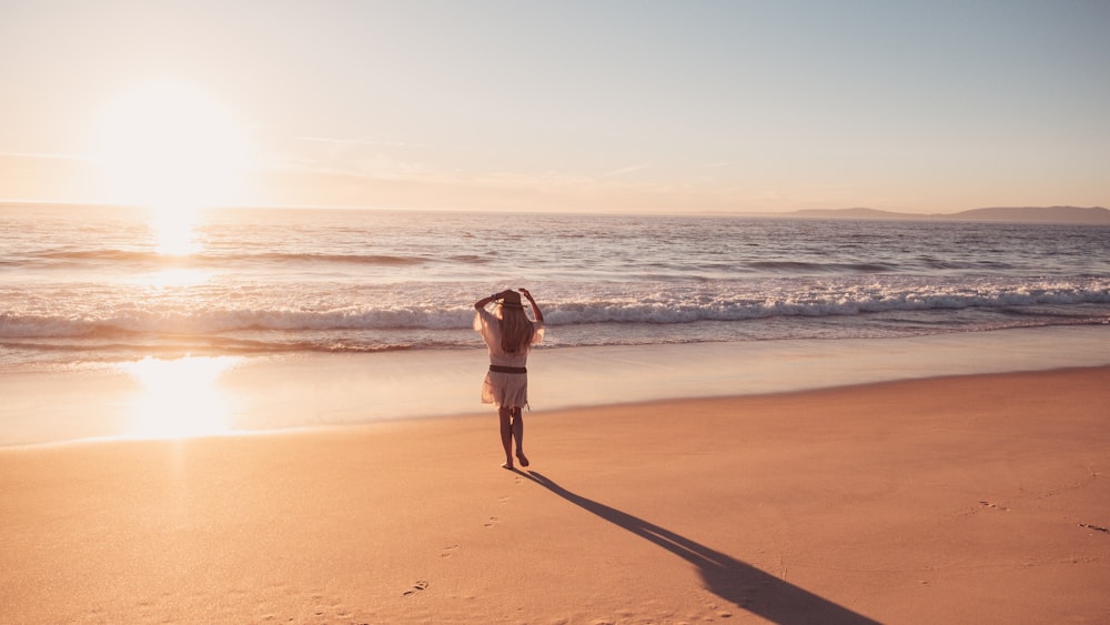 Une femme debout au sommet d’une plage de sable au bord de l’océan