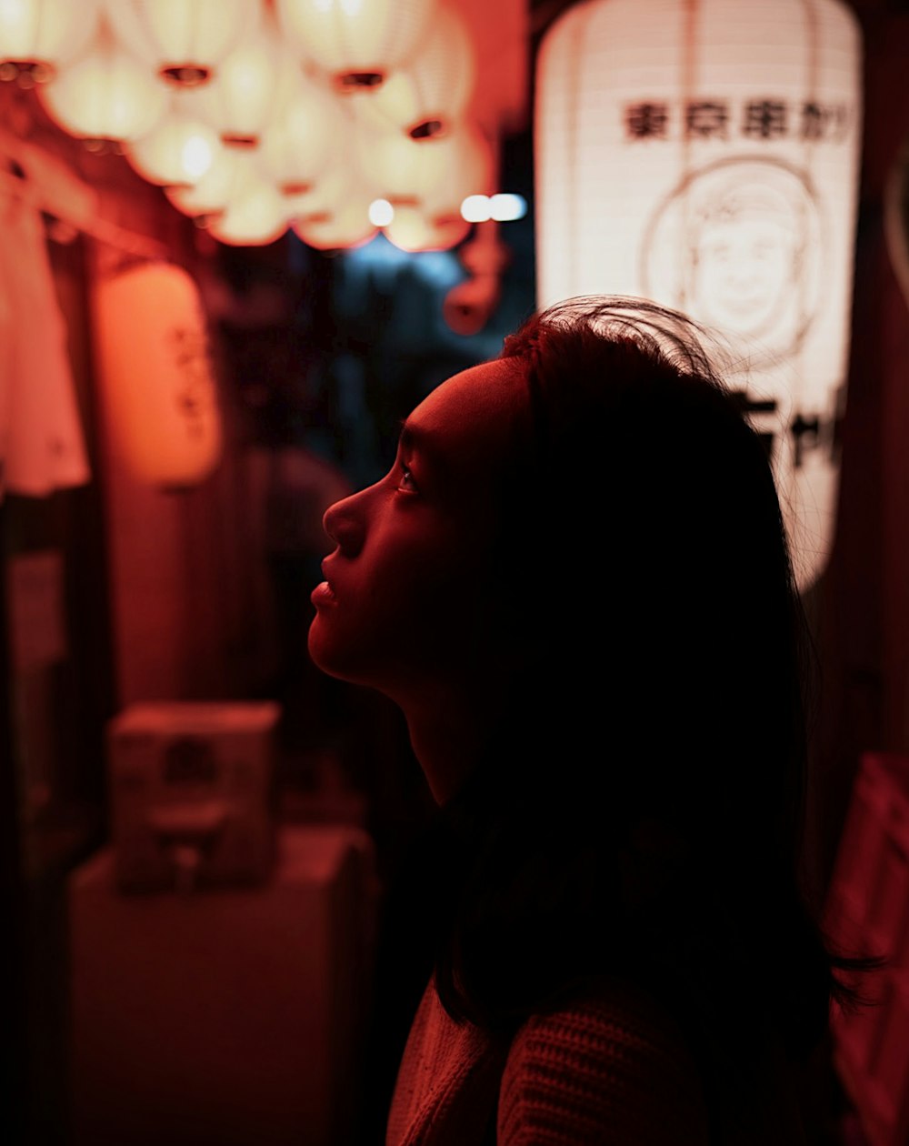 a woman standing in a dark room with a chandelier hanging from the ceiling