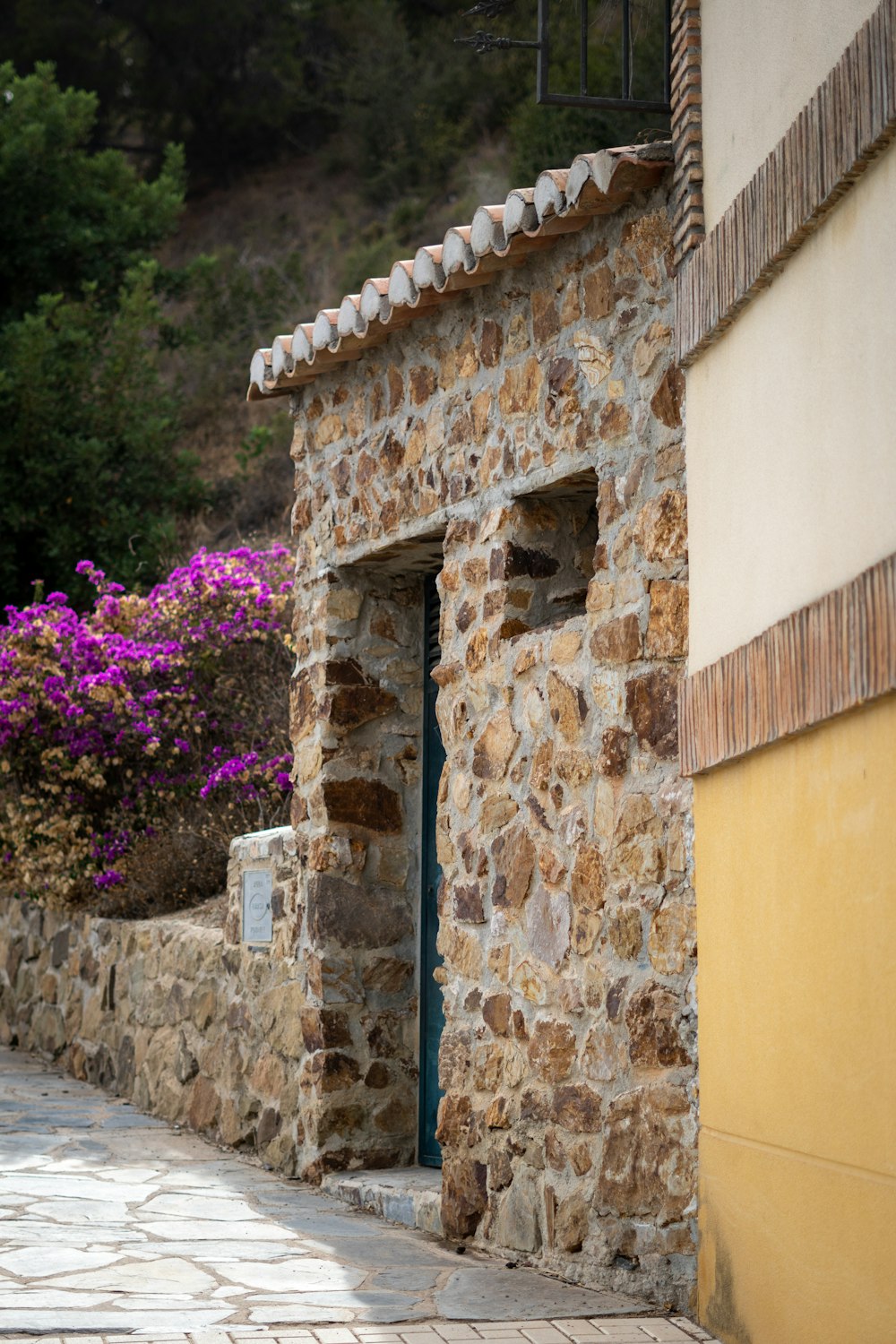 a stone building with a blue door and purple flowers