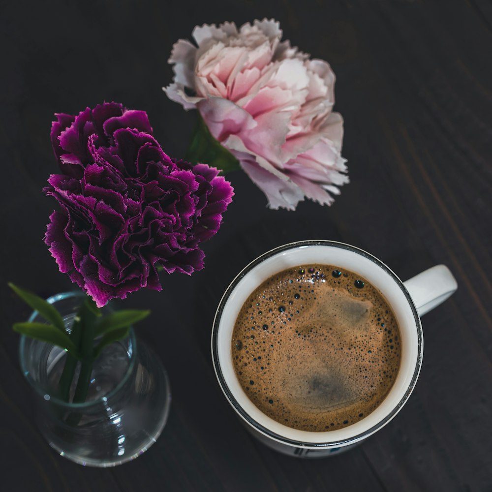 a cup of coffee next to a vase of flowers