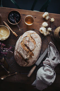 Artisan bread loaf with a golden crust resting on a linen cloth beside a jar of homemade jam